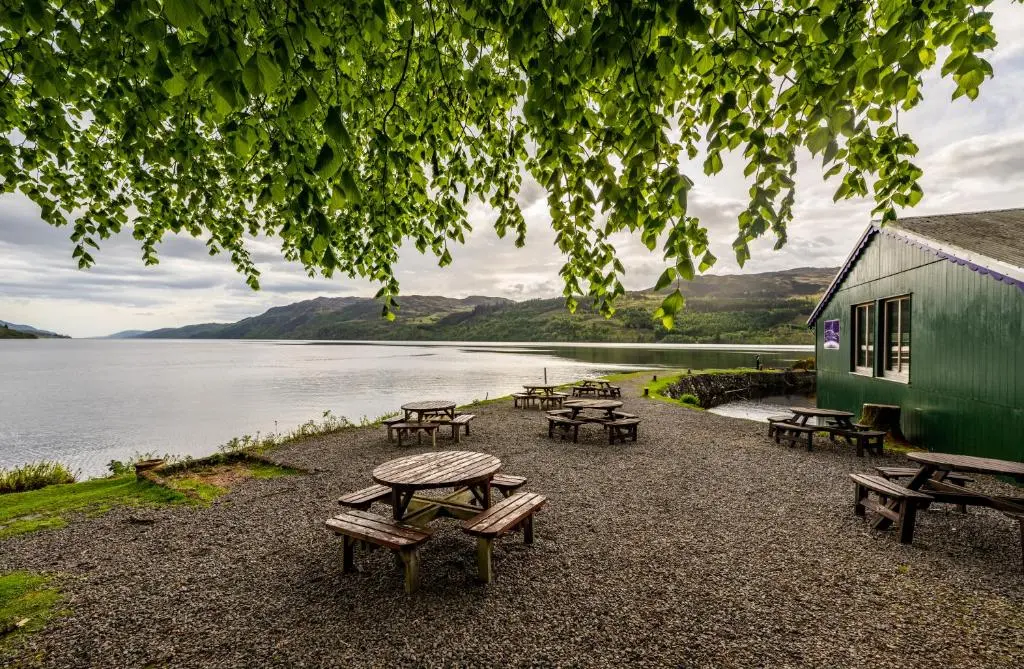 a group of picnic tables and benches next to a lake at The Livingstone Loch Ness OS9 in Fort Augustus