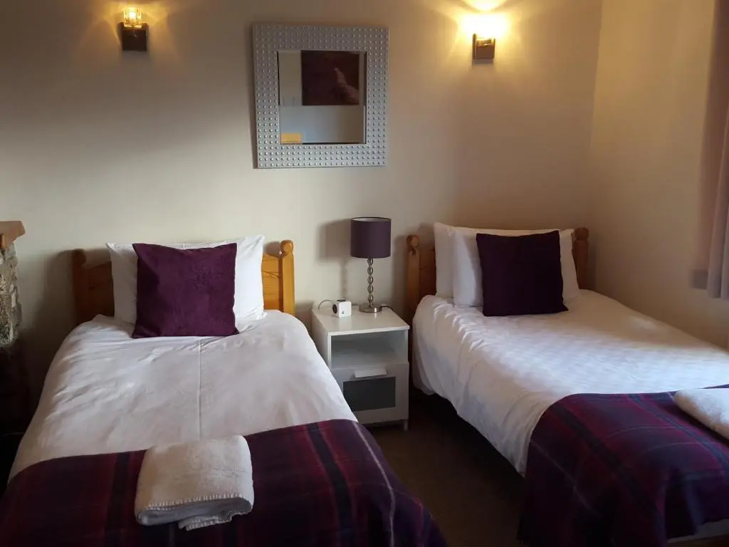 a room with two beds and a lamp on a table at Carn Mhor Bed and Breakfast in Aviemore