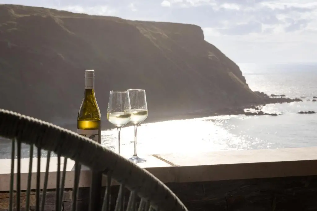two wine glasses and a bottle on a balcony overlooking the ocean at Muckle View in Gardenstown