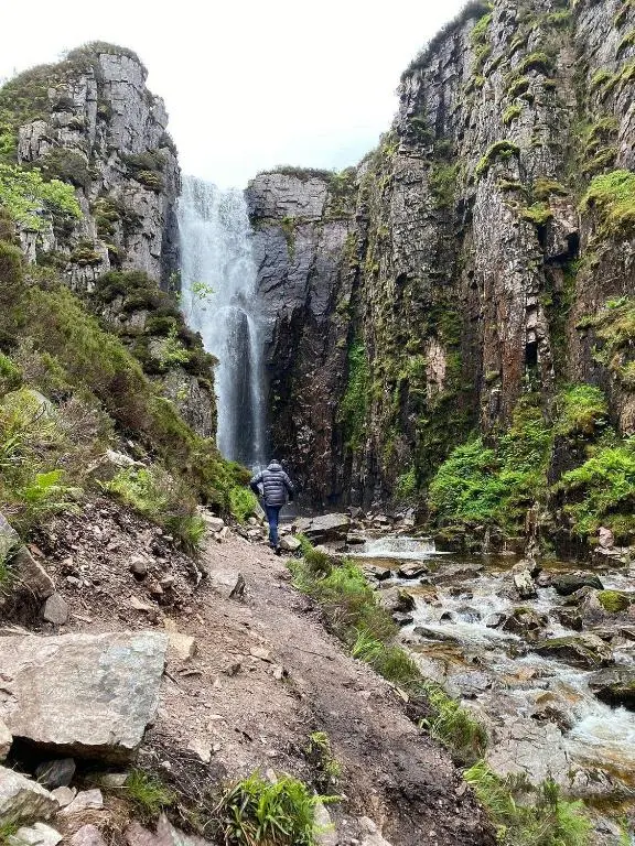 a person walking down a path in front of a waterfall at Phils House in Lairg