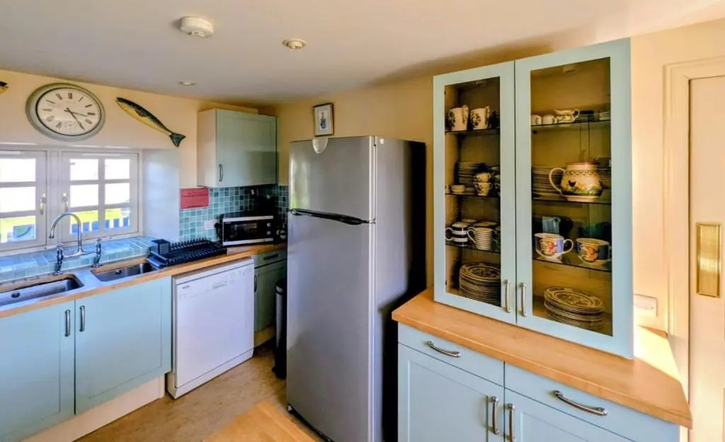 a kitchen with a refrigerator and a clock on the wall at Reids Cottage in Lairg