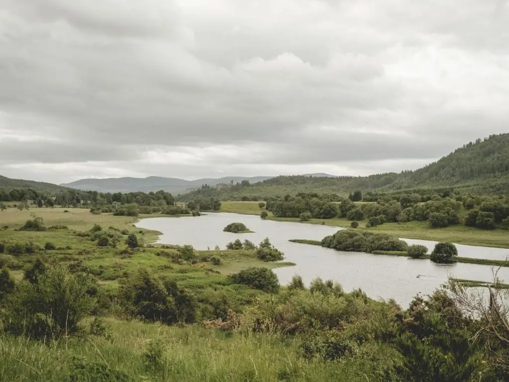 a river in a field with mountains in the background at Reids Cottage in Lairg