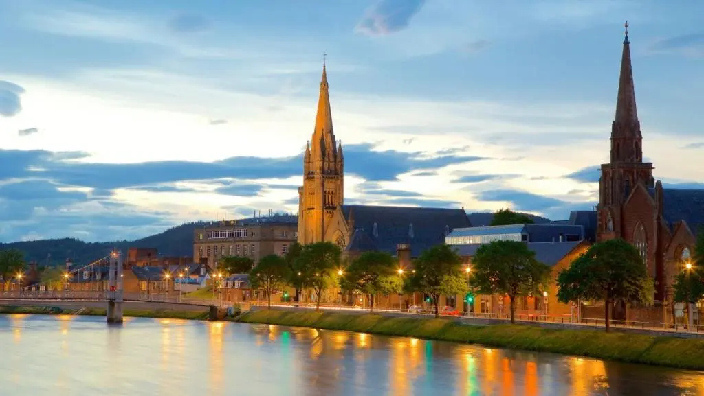 a large building with a clock tower next to a river at The Wee Heilan' Drochaid in Inverness