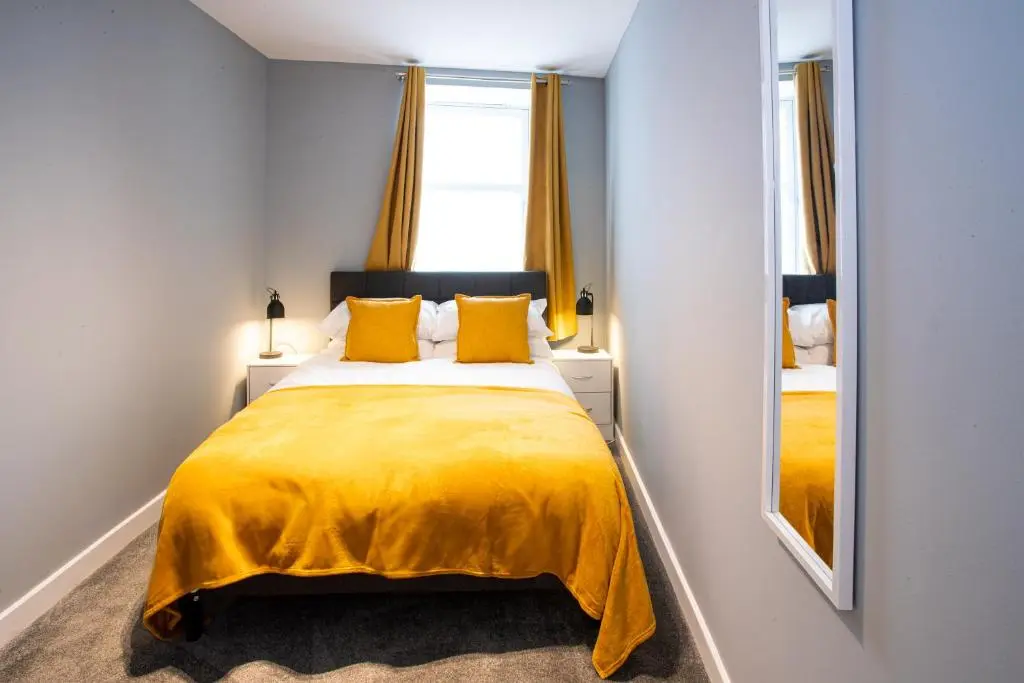 a bedroom with a bed with a yellow blanket and a mirror at Baron Taylor Stays in Inverness