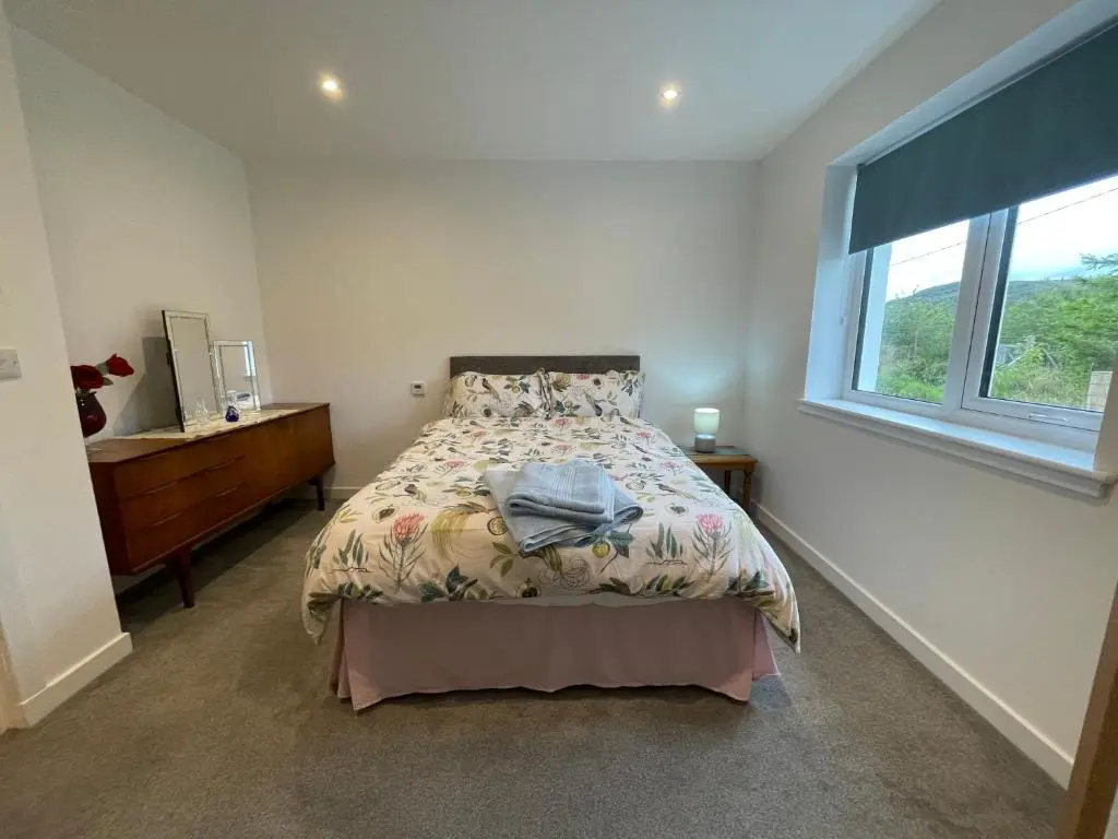 a bedroom with a bed and a dresser and a window at Fionnlagh Cottage in Eskadale