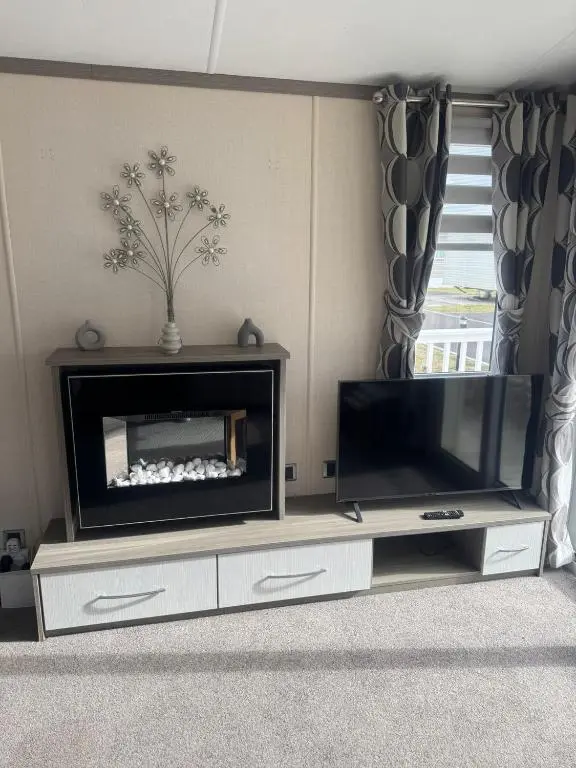 a living room with a flat screen tv on a entertainment center at Spacious Modern Seaside Caravan in Lossiemouth