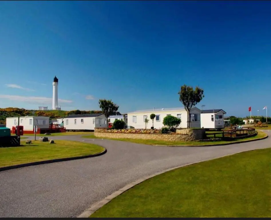 a winding road with a lighthouse in the background at Spacious Modern Seaside Caravan in Lossiemouth