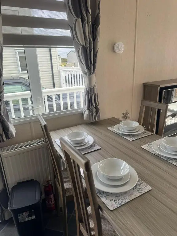 a dining room table with plates and chairs and a window at Spacious Modern Seaside Caravan in Lossiemouth