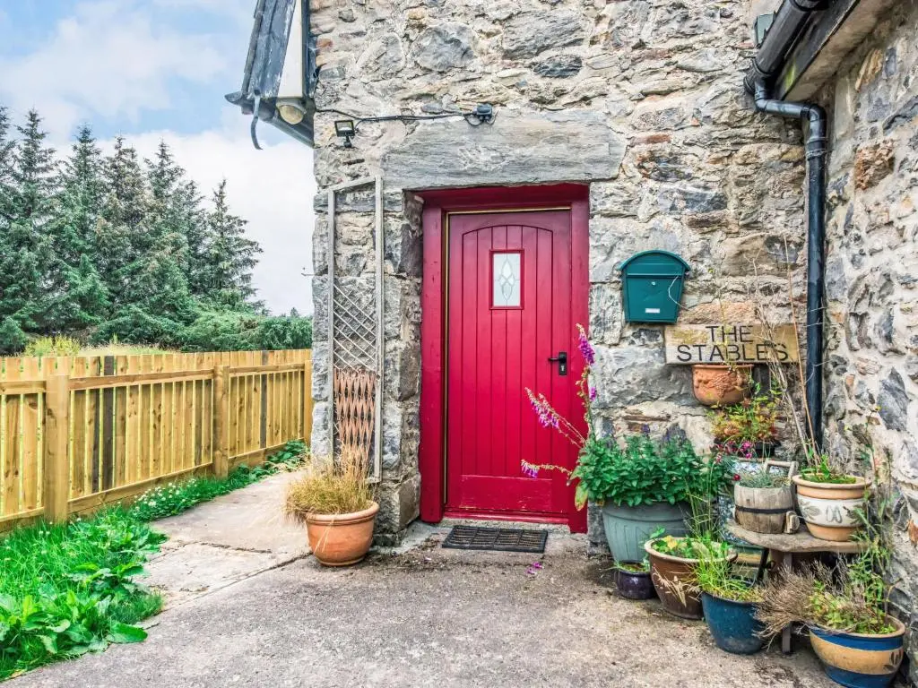 a red door on a stone building with potted plants at Holiday Home Highland View by Interhome in Drumnadrochit