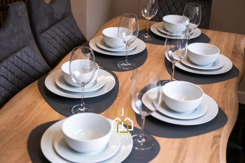 a wooden table with plates and wine glasses on it at Fraserburgh Residence - SJA Stays - Modern 3 Bed Apartment in Fraserburgh