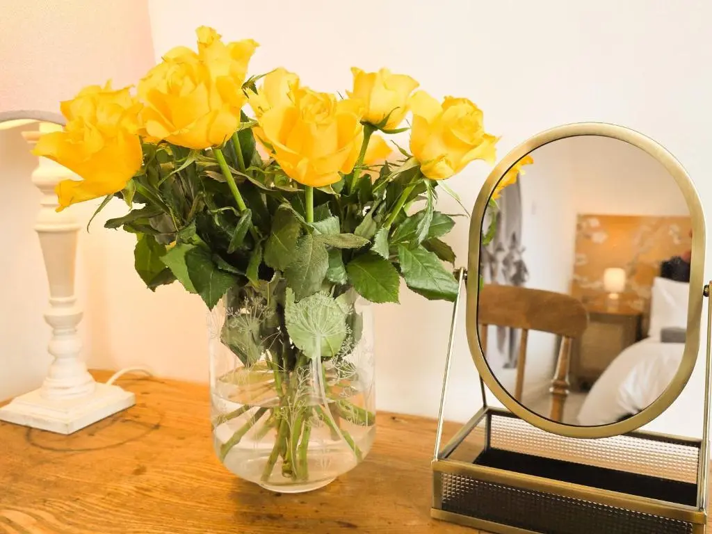 a vase of yellow flowers on a table next to a mirror at 18 Dalfaber Park- with hot tub in Aviemore in Aviemore