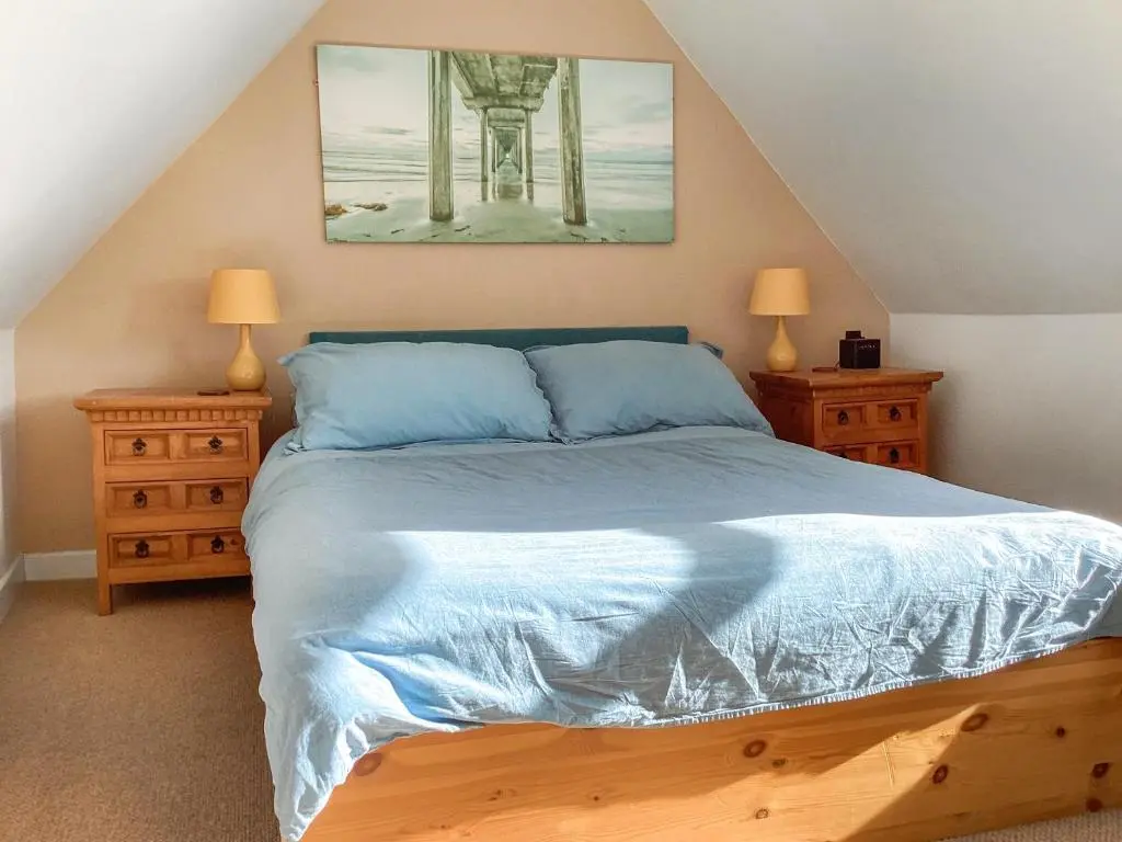 a bedroom with a bed with blue sheets and two night stands at Old Laurel Cottage in Jemimaville