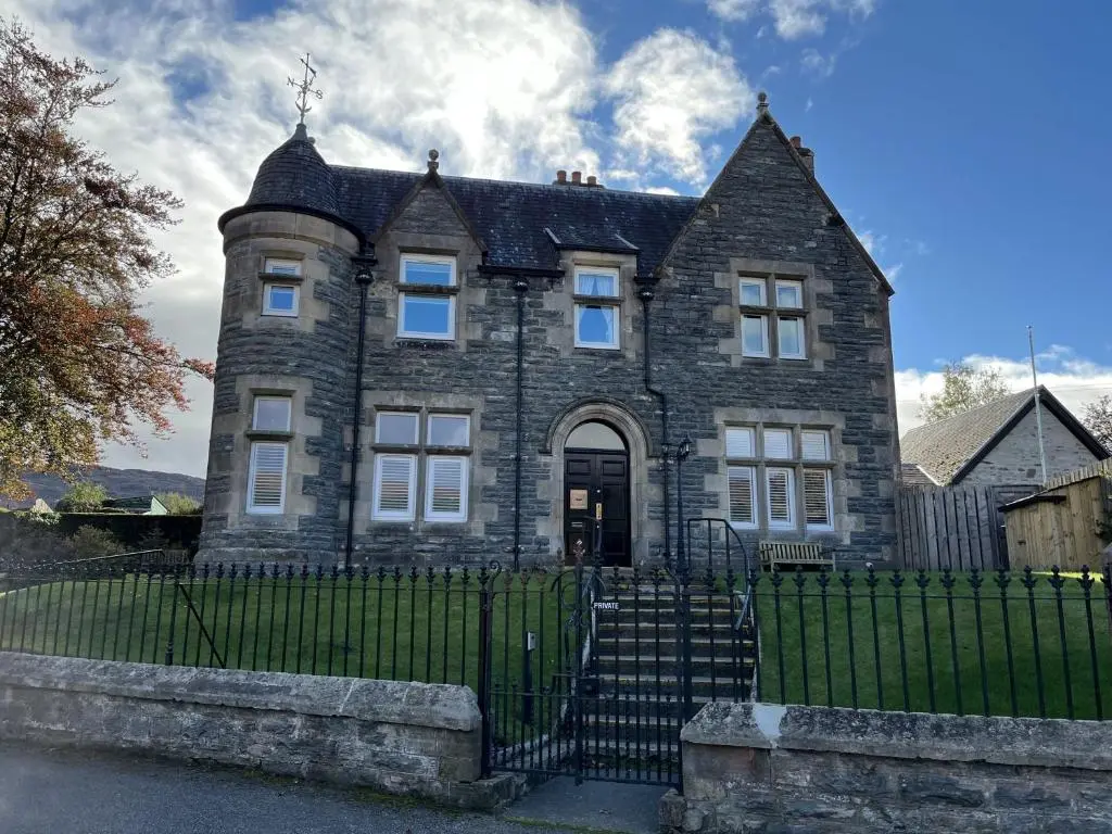 an old stone house with a black fence at Bank House apartment in Fort Augustus