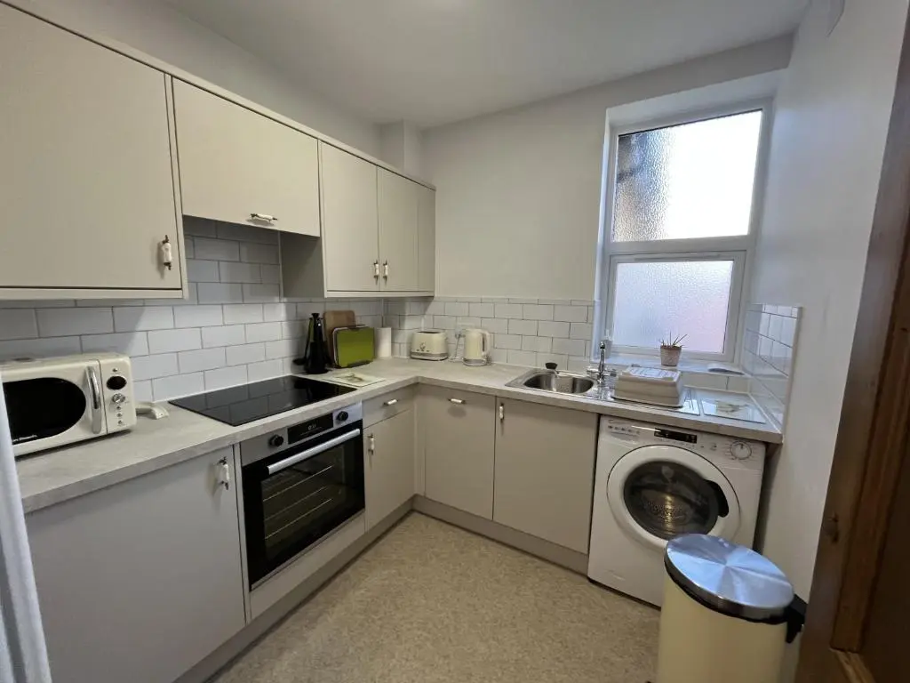 a kitchen with white cabinets and a washer and dryer at Bank House apartment in Fort Augustus