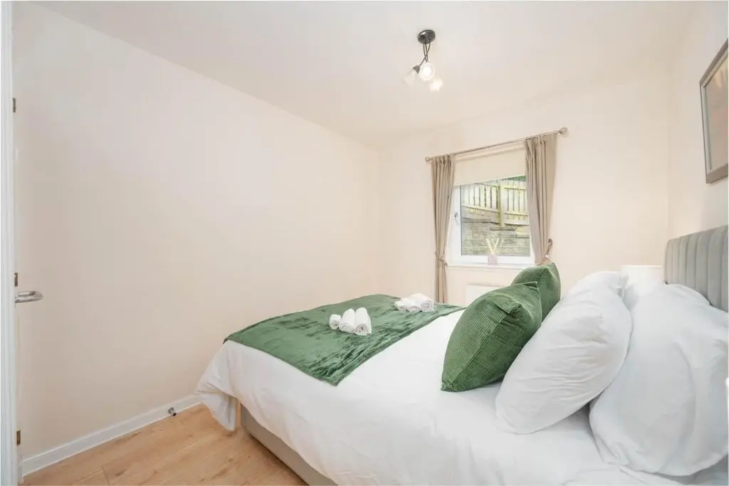 a white bed with green and white pillows and a window at Aberdeen 2BR Flat Near Airport & City Centre in Aberdeen