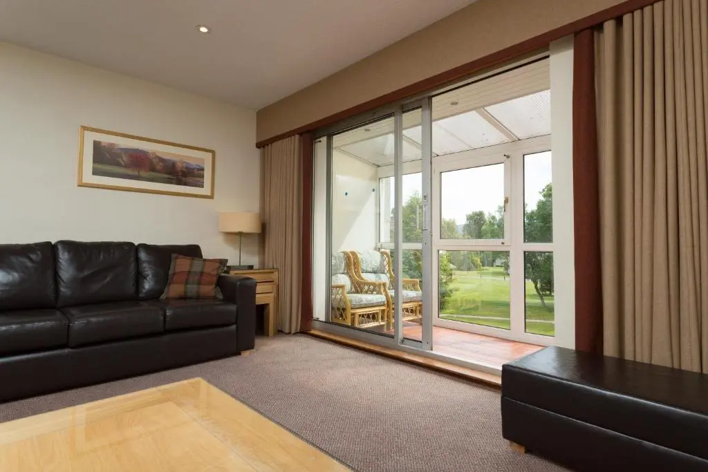 a living room with a black couch and a sliding glass door at Macdonald Spey Valley Resort in Aviemore
