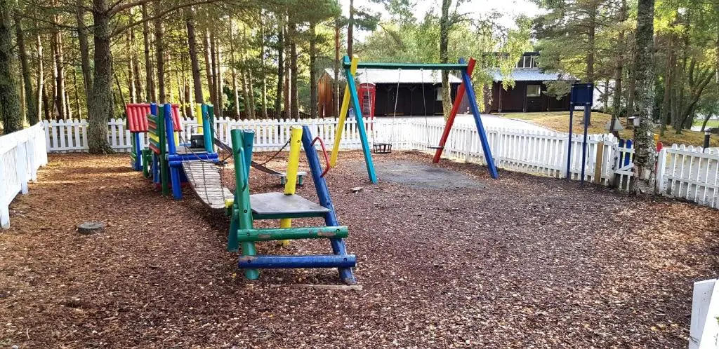 a playground with colorful swings and a white fence at Macdonald Lochanhully Resort in Aviemore
