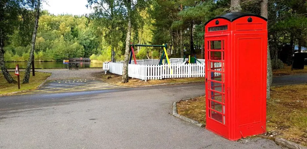 a red phone booth in a park with a playground at Macdonald Lochanhully Resort in Aviemore