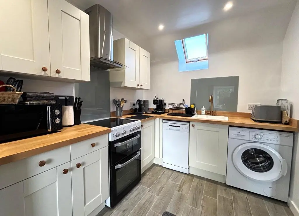 a kitchen with white cabinets and a washer and dryer at Smiddy Cottage in Portmahomack