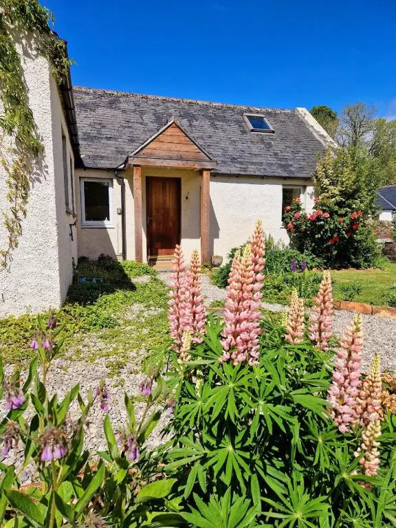 a house with a bunch of flowers in front of it at Highland River Cottage with Hot Tub in Evanton