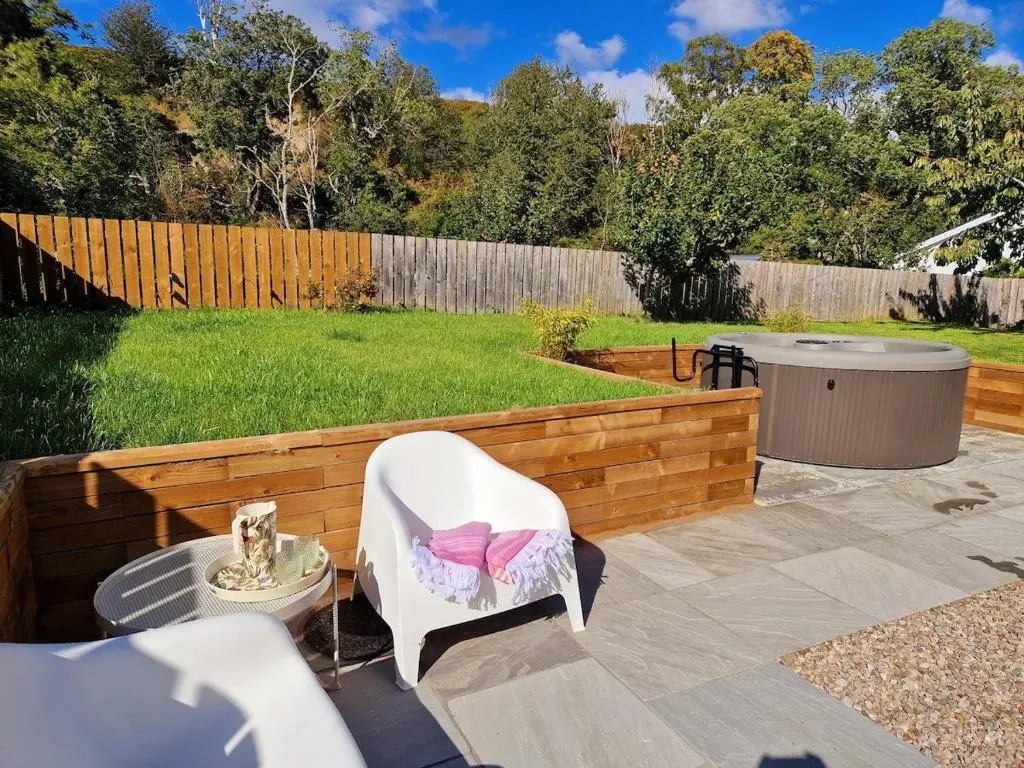 a patio with a white chair and a fence at Highland River Cottage with Hot Tub in Evanton