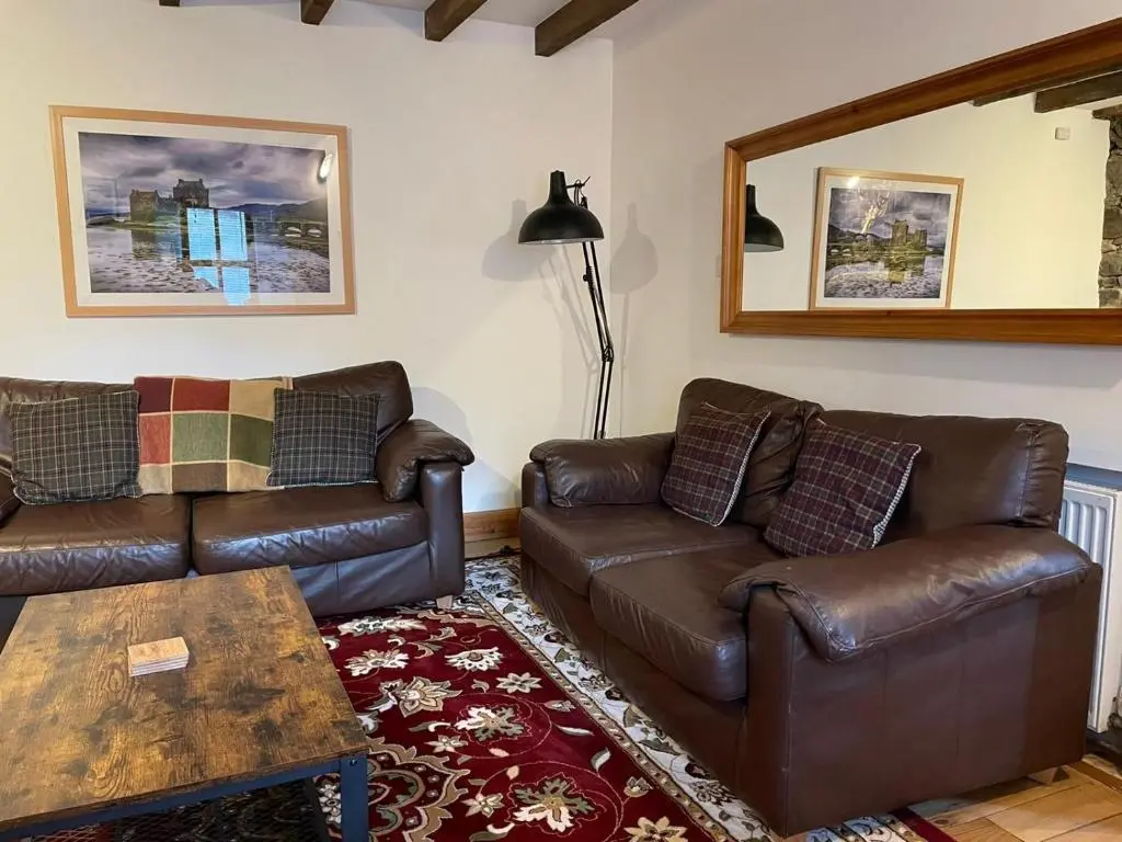 a living room with two leather couches and a table at Culrain Cottage in Fort Augustus