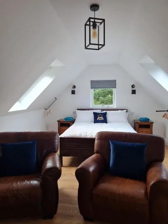 a bedroom with a bed and two leather chairs at Woodland studio in Stittenham