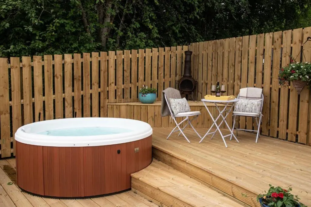 a hot tub on a deck with a table and chairs at Beautiful dog friendly lodge with hot tub in Aboyne