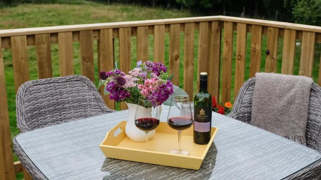 a table with two glasses and a bottle of wine and flowers at Beautiful dog friendly lodge with hot tub in Aboyne