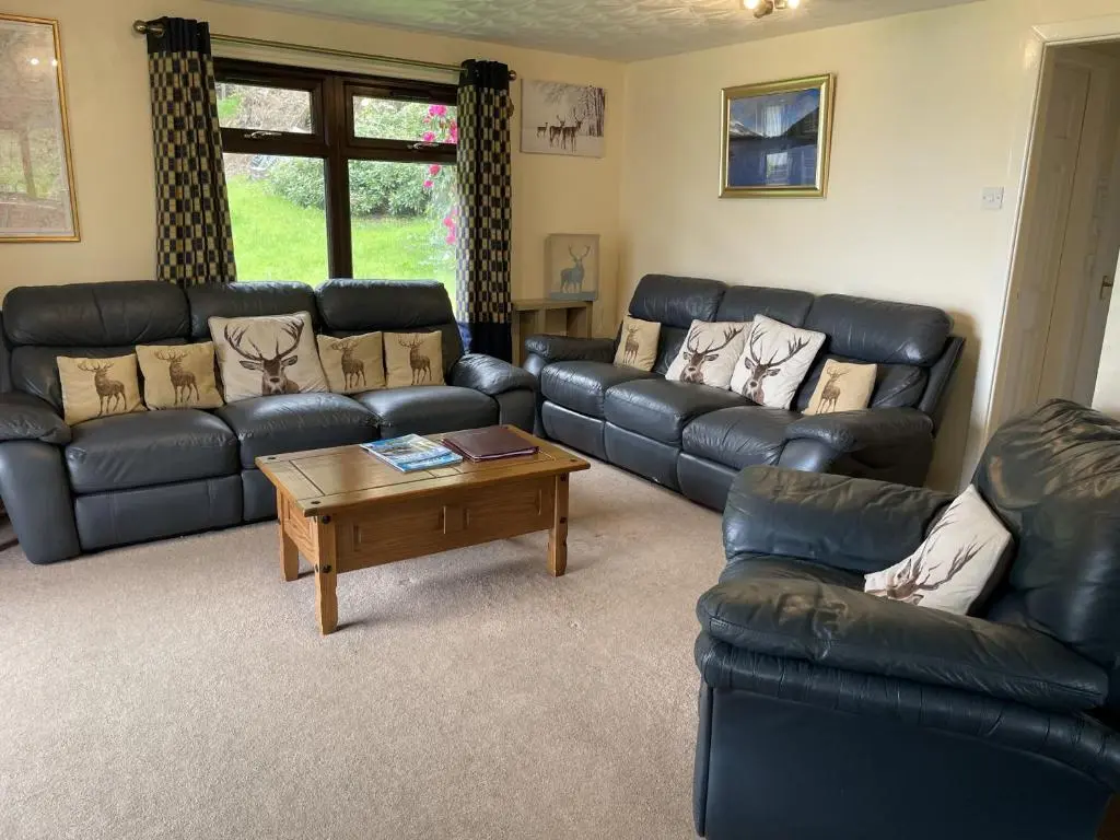 a living room with black leather couches and a coffee table at Mountain Thyme Lodge in Kilfinnan