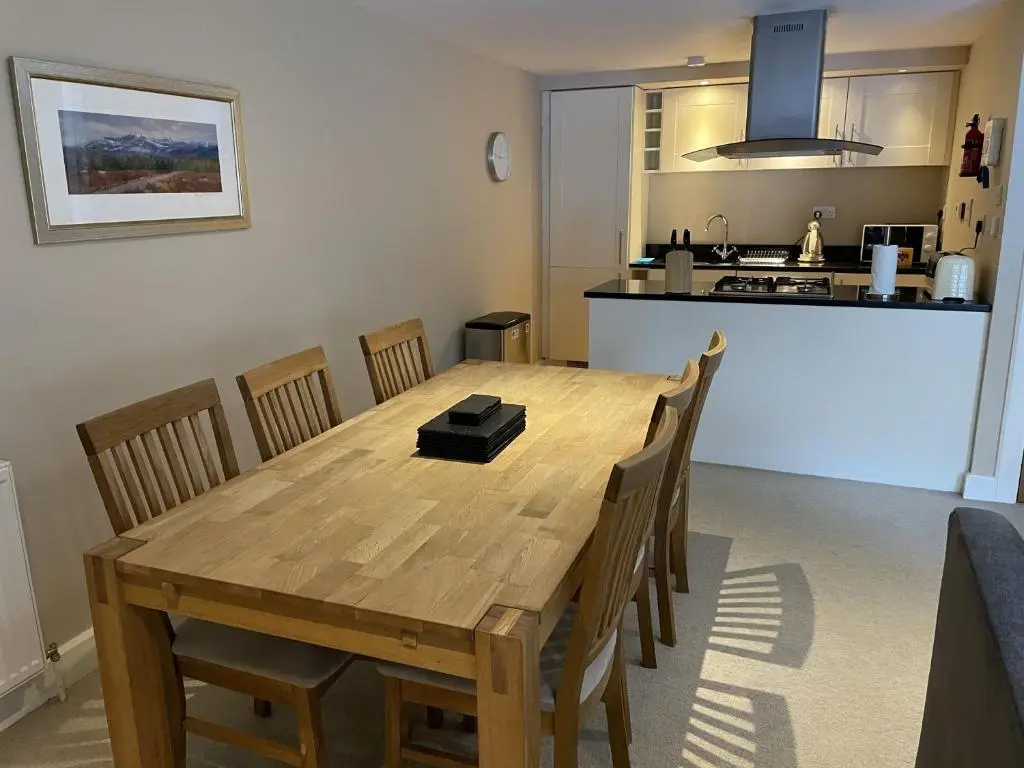 a dining room table with chairs and a kitchen at Raven Wing 11 - Kintail Apartment in Fort Augustus