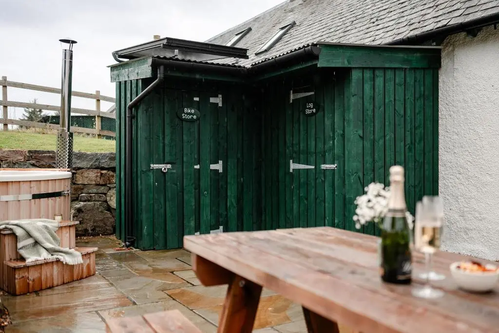 a green shed with a wooden table in front of it at Garradh Cottage - Seasgair Lodges in Kincraig