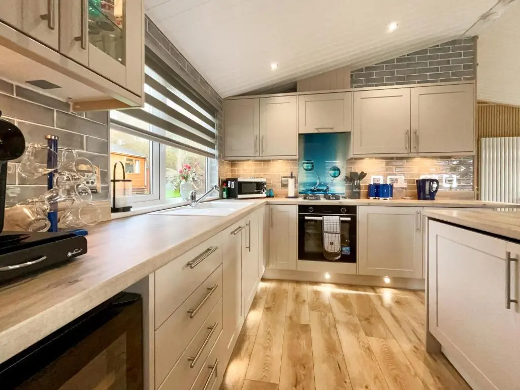 a kitchen with white cabinets and a wooden floor at Haven Lodge - Uk50792 in Banchory