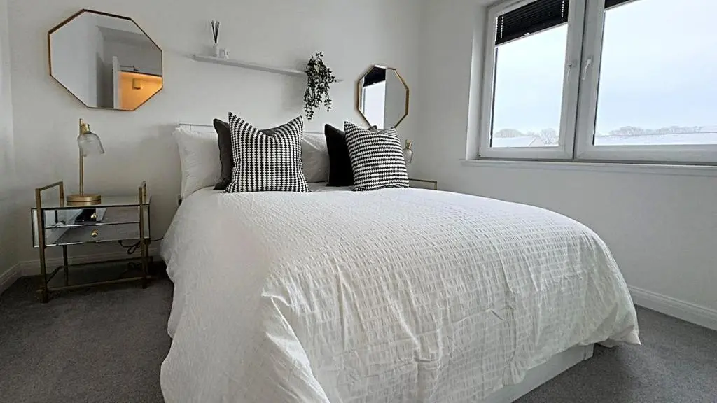 a bedroom with a white bed with pillows and a mirror at High-Ness View in Inverness