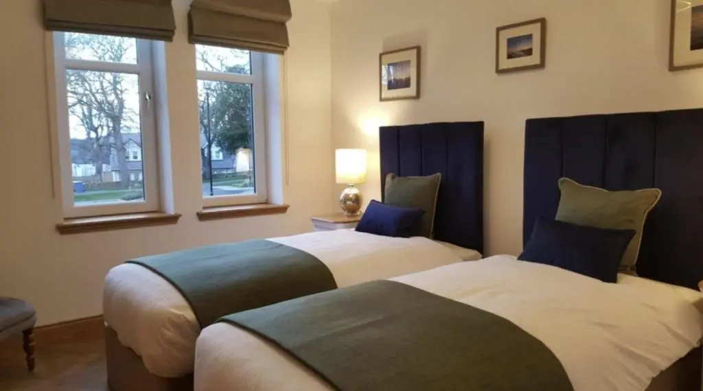 two beds in a room with two windows at Royal Gardens Apartment 2 in Dornoch