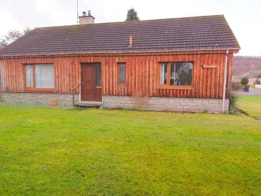 a wooden house with a grass yard in front of it at Loramore in Aviemore