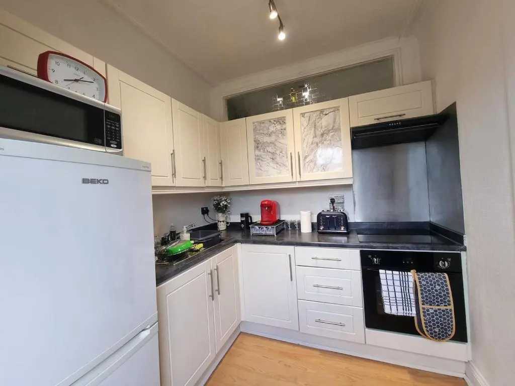 a kitchen with white cabinets and black appliances at 2 bedroom flat- 5 minutes walk from city centre in Inverness