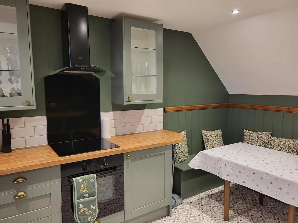 a kitchen with green walls and a table and a bench at Gardeners Cottage