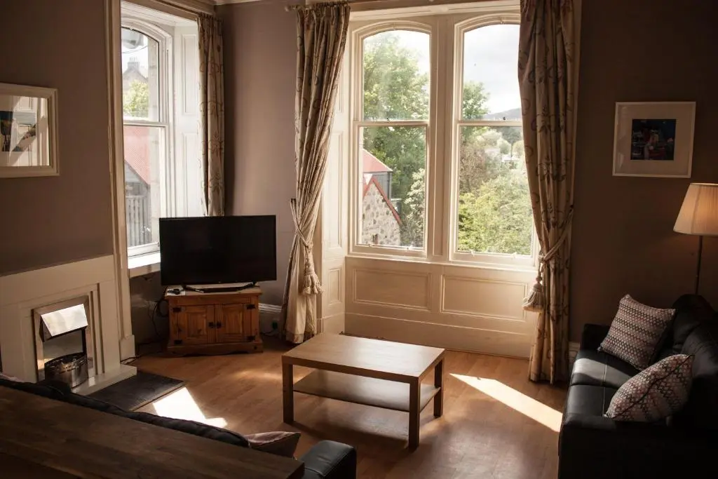 a living room with a couch and a tv and a window at Auld Bank House in Braemar
