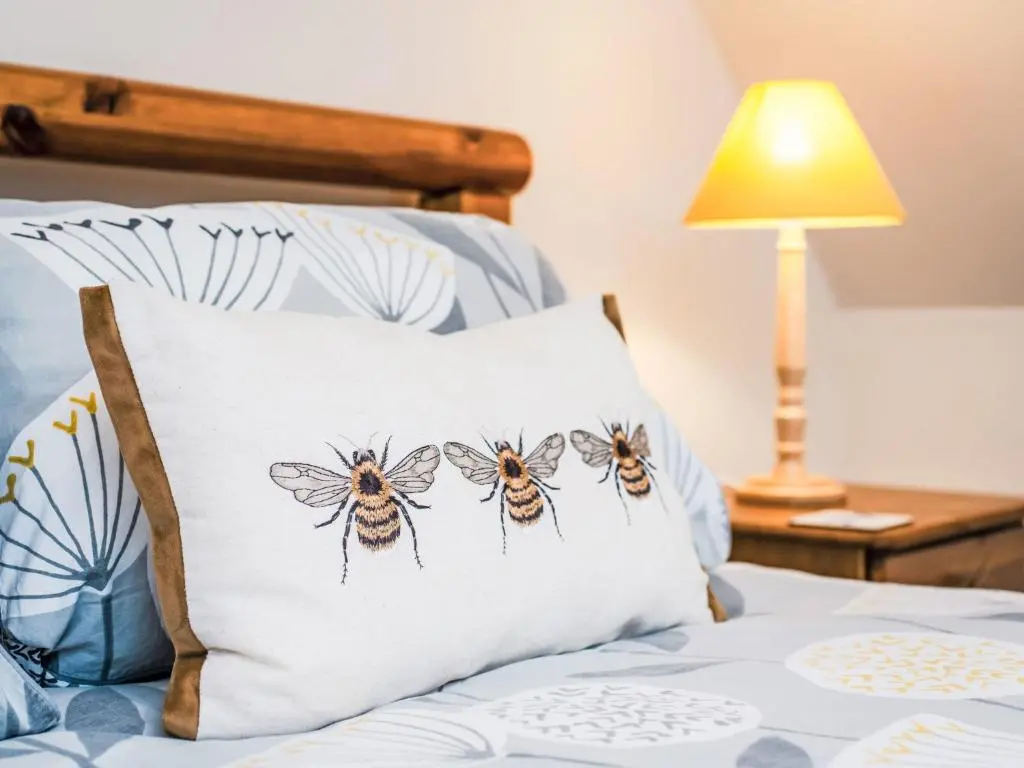 a bed with a pillow with three bees on it at Holiday Home Wester Bunloit by Interhome in Drumnadrochit