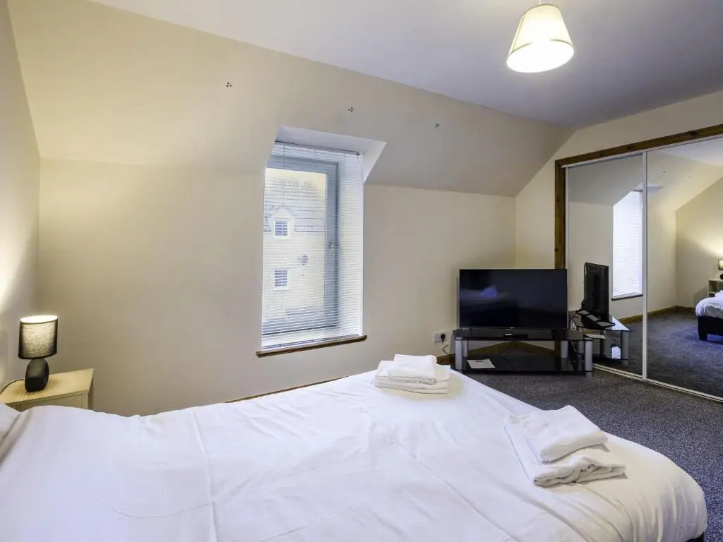 a bedroom with a large white bed and a television at Apartment Pitgaveny Apartment by Interhome in Lossiemouth