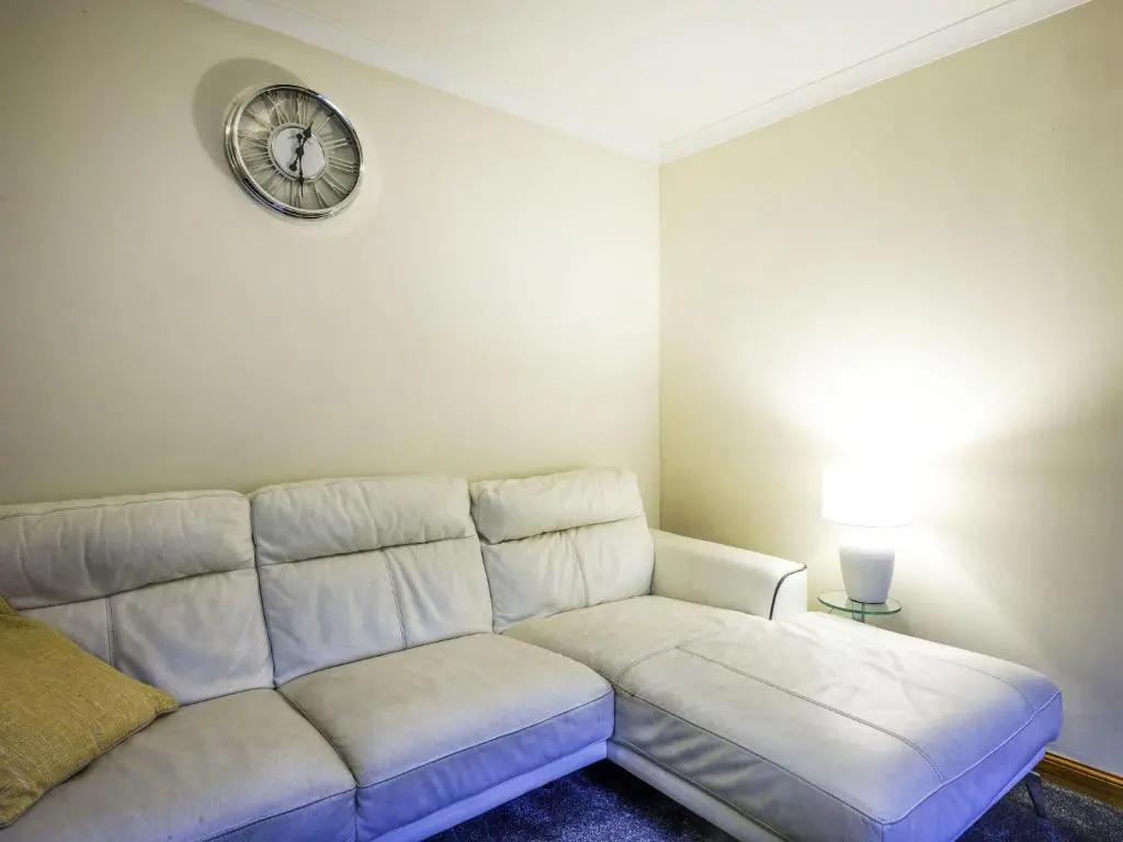a white couch in a living room with a clock on the wall at Apartment Pitgaveny Apartment by Interhome in Lossiemouth