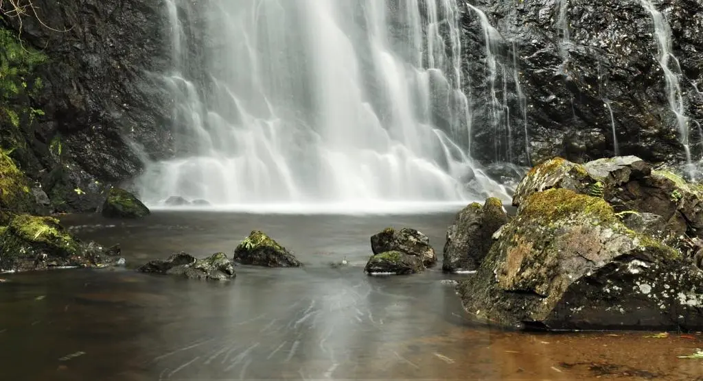 a waterfall with rocks in front of a waterfall at Ardachy Riverside Accessible One bedroom Holiday let in Fort Augustus