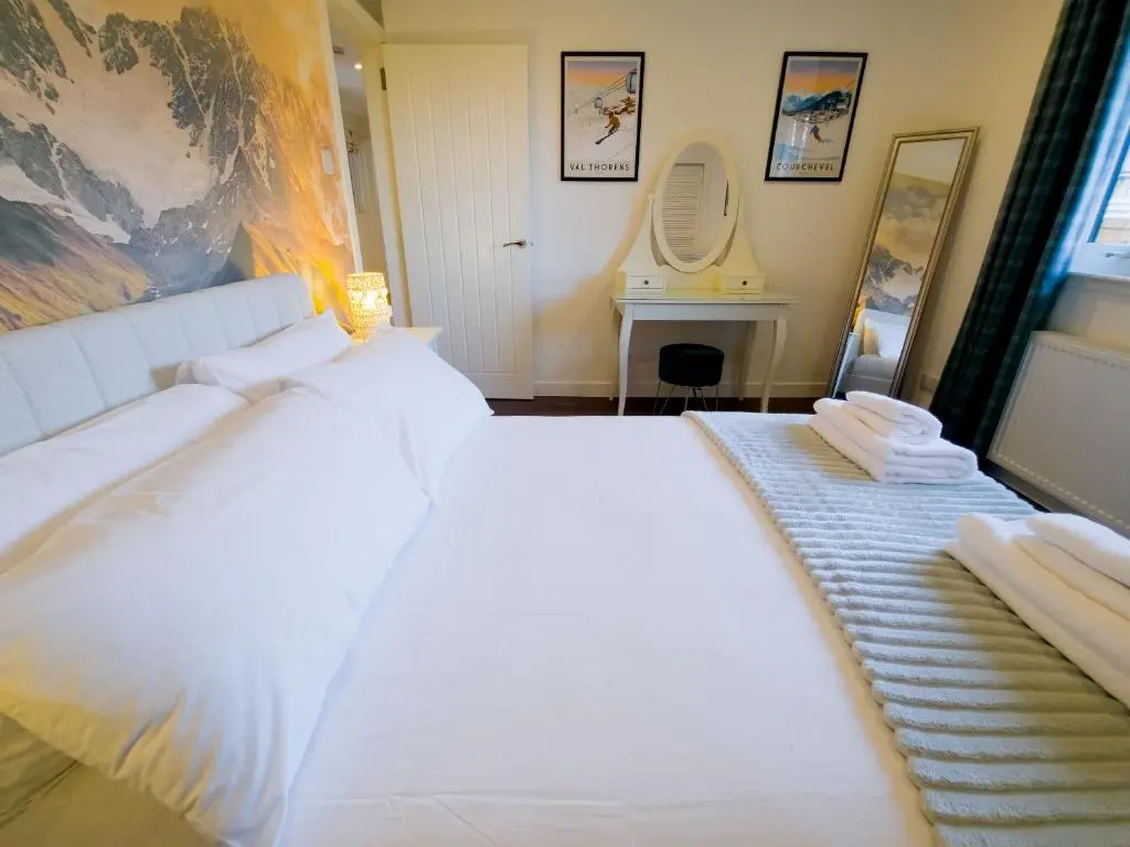 a bedroom with a large white bed and a mirror at Woodland House in Tomatin