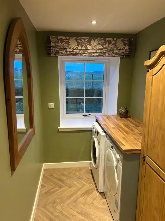 a laundry room with a washing machine and a window at Calsie Cottage, Clatt in Kirktown of Clatt