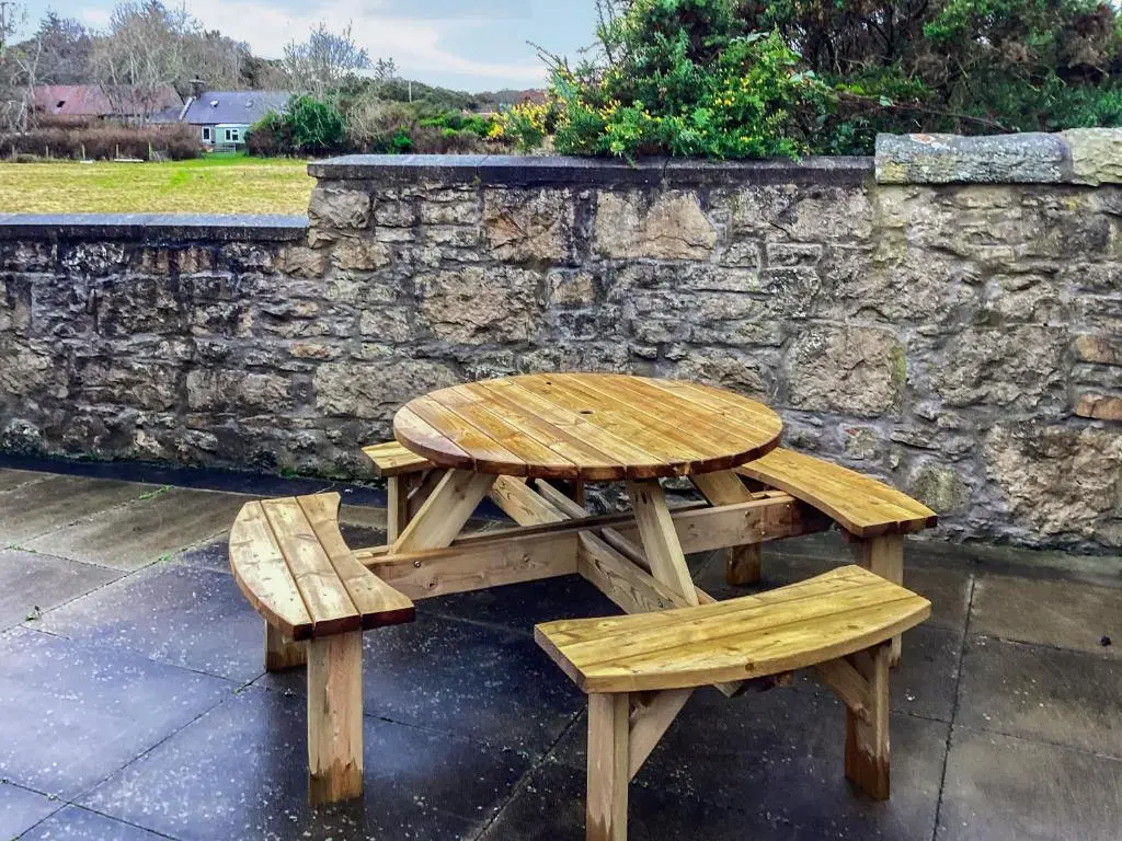 a wooden picnic table and benches next to a stone wall at Mirodon in Brora