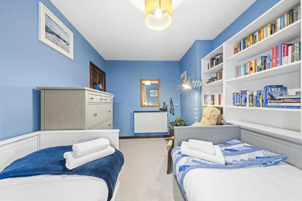 two beds in a room with blue walls and bookshelves at Beinn View 3 Bedroom House - Sea View - Ardersier in Ardersier