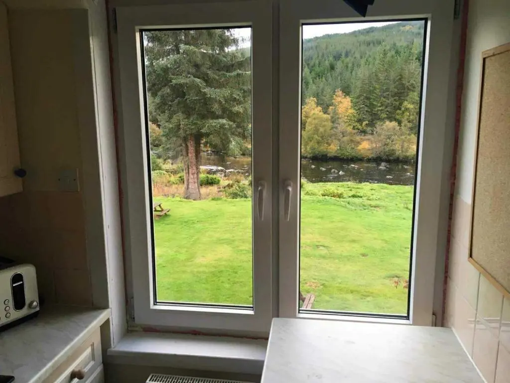 two windows in a kitchen with a view of a field at River View in Garve