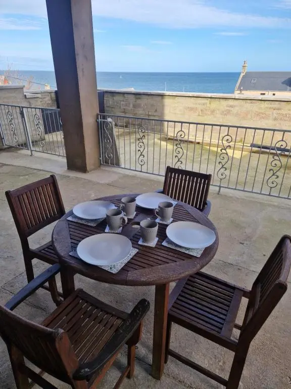 a wooden table with plates and cups on a balcony at Rook View, Modern Coastal Retreat with Free Parking in Buckie