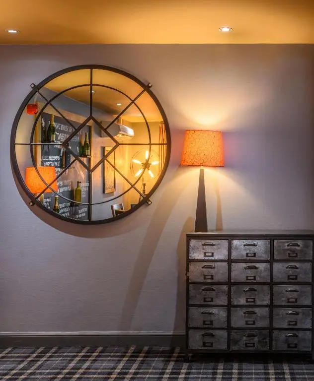 a mirror on the wall next to a dresser and a lamp at The Dunavon in Dyce
